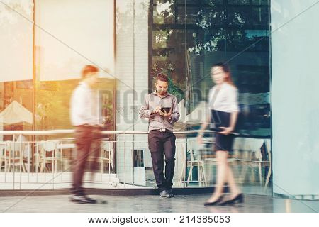 Businessman using a digital tablet office outdoors and Blurred People Walking in Front of Modern Office Building