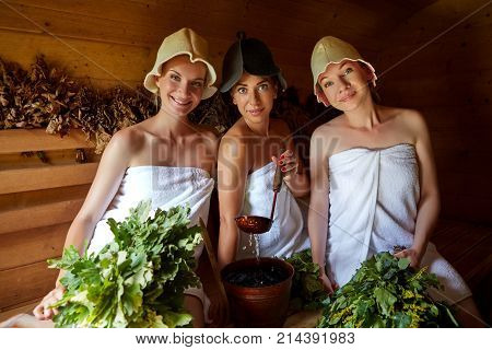 three beautiful young women in towels realxing in wooden sauna. inside shot with natural light.