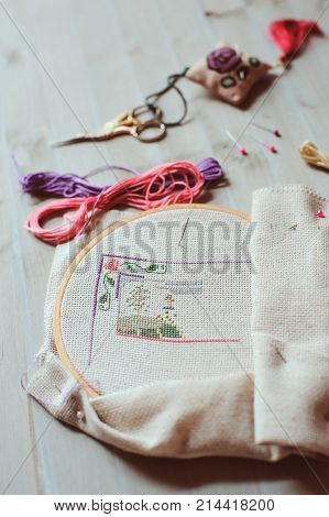 cross stich set in process. hoop with embroidered pattern scissors canvas and colorful yarn. Selective focus. Handmade and hobby concept.