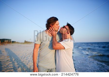 Two men embrace against the background of the sea. They represent a playful kiss.