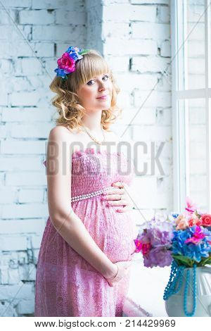 Pregnant woman smiling, looking at belly, holding flowers. Pink dress