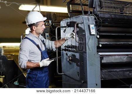 Middle-aged worker in uniform holding digital tablet and consulting about service of industrial machine online