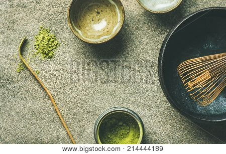 Flat-lay of Japanese tools for brewing matcha green tea. Matcha powder in tin can, Chashaku spoon, Chasen bamboo whisk, Chawan bowl and cups over grey concrete background, top view, copy space