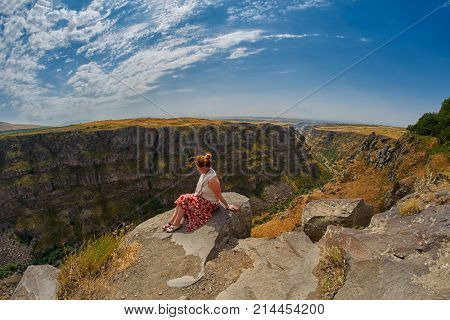 Young woman sitting on the edge of Kasagh river gorge near Saghmosavank monastery