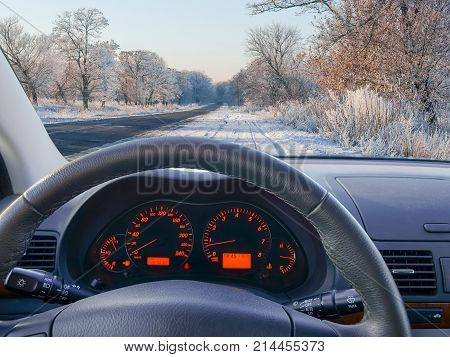 View to road through the windshield of the car standing by the roadside with dashboard and steering wheel on a foreground in winter