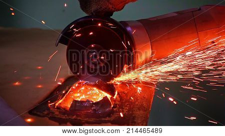 Cutting metal with disc grinder abrasive saw producing bright colorful sparks. Worker cuts metal with hand electric tool.
