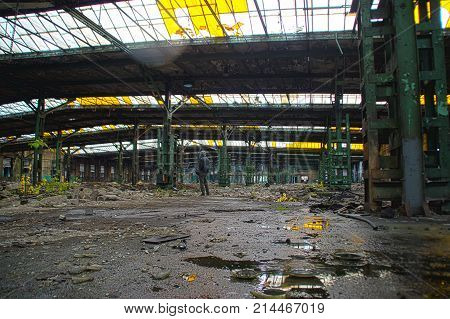 Abandoned old factory hall with windows in roof. Man in large space in forgotten industrial interior.