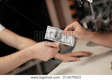 A young man gives money to another man. They are in the store. The buyer has cash in his hand.