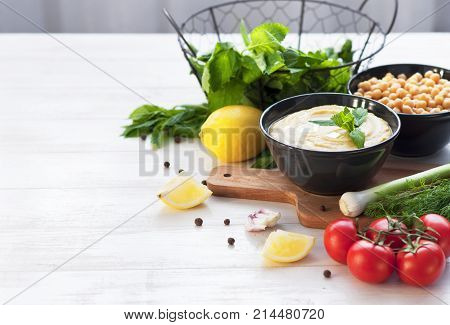 Bowl with hummus, chickpeas, lemon, cherry tomatoes and herbs on a white rustic wooden background.
Middle Eastern cuisine. Background hummus with place for text.