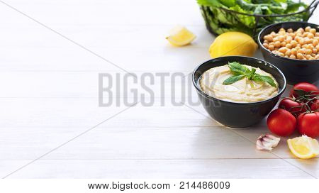 Bowl with hummus, chickpeas, lemon, cherry tomatoes and herbs on a white rustic wooden background.
Middle Eastern cuisine. Background hummus with place for text.