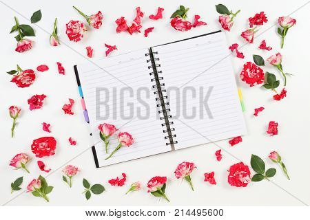 Open paper notebook and rose flowers frame on white background. Flat lay, top view