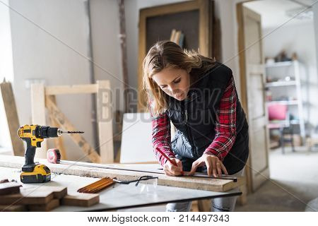 Young woman worker in workroom. Female carpenter measuring wood plank.