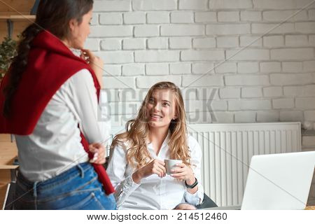 Gorgeous young woman having cup of coffee while working with her female colleague discussing business copyspace teamwork communication partnership meeting ideas success project startup.
