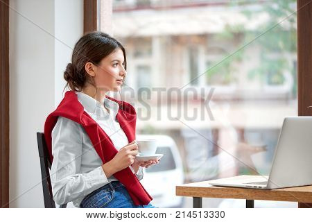 Shot of a young attractive woman having coffee at the cafe sitting relaxed looking at the window copyspace laptop computer technology connectivity mobility wireless project morning businesswoman.