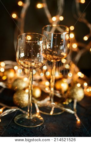 Two glasses for wine and golden Christmas balls against a background of blurred golden lights. Shallow depth of field.