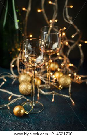 Two glasses for wine and golden Christmas balls against a background of blurred golden lights. Shallow depth of field.