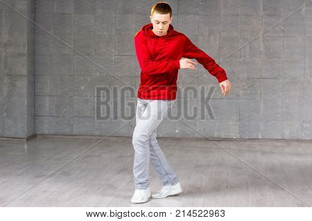 Young male modern dancer dancing. Modern style dancer in red sweater dancing brake dance over grey background. Young talented freestyle dancer.