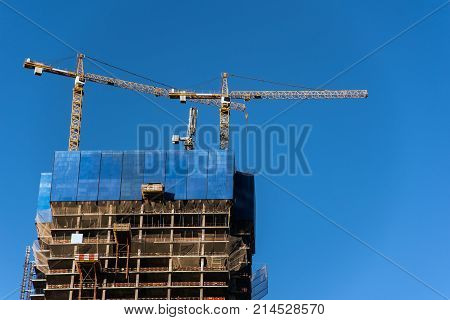 Industrial construction tower cranes and high-rise building under construction against blue sky