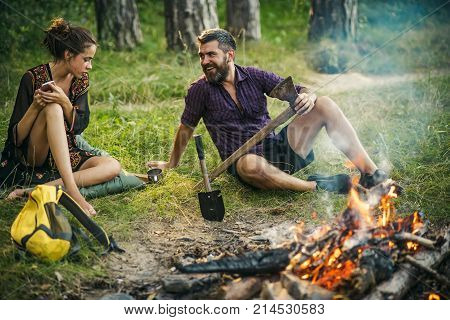 Camping hiking summer vacation. Man hipster smile with axe. Girl or woman use mobile phone. New technology or archaism concept. Couple of hikers relax at bonfire in forest.