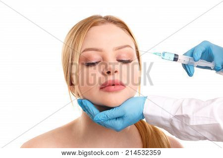 The doctor's hands in a white coat and in medical gloves make an injection in the eyebrow area of an attractive woman. Isolated on white background.