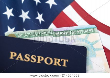 United States of America permanent resident card green card displayed with a US flag in the background and a passport in the foreground. Immigration concept. Close up with shallow depth of field.