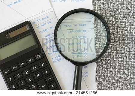 Financial office salary man or tax calculation concept as black calculator and magnifying glass with numbers on carbon salary slips.