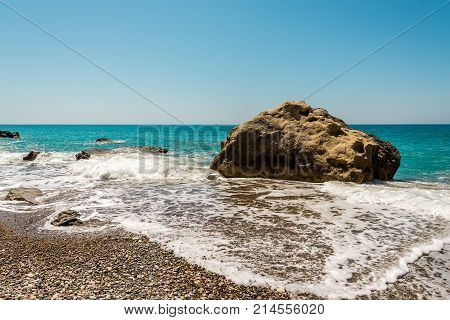 A Large Rock Surrounded By Water At Pissouri Pebble Beach, Cyprus
