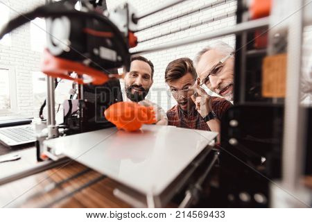 Three men are working to prepare printed model on the 3d model of the heart. They are satisfied with the result. They peer through the working field 3e of the printer.
