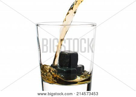 Whiskey pours into a glass with stones.
