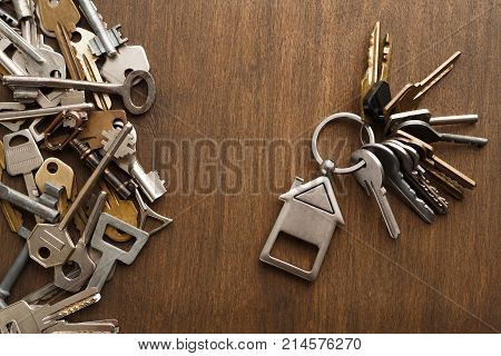 Bunch of keys with house shaped trinklet against wooden background and collection of different keys. Safety, security and real estate concept, top view, copy space