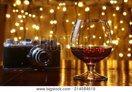 Glass of brandy or cognac and retro camera on the wooden table.