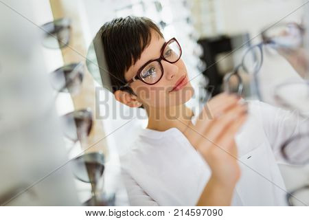 Pretty young woman is choosing new glasses at optics store to correct eyesight