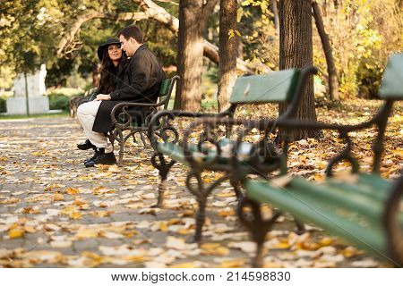 Beautiful gourgeous couple sitting on a bench in autumn park