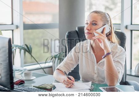 Girl in the office have mobile conversation and recording information.