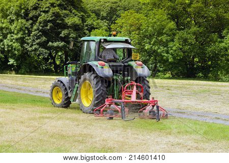 Llangollen Wales UK - July 5 2017: Tractor working in a field with a twin rotor hay turner or tedder attachment a device for turning cut grass or hay