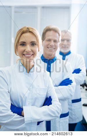 Professionals in genetics. Cheerful professional experienced researchers smiling and wearing uniforms and standing one by one in the lab