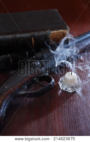 Extinguished candle with smoke near old shotgun and book