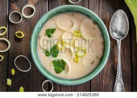 Bowl of yummy potato soup with leek on wooden table, top view