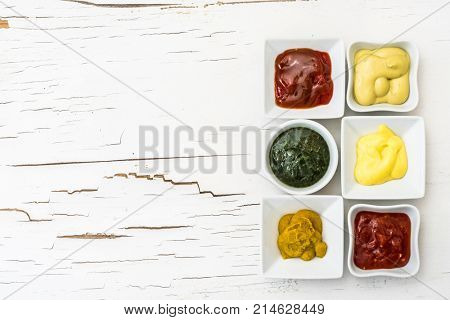 Classic set of sauces in square white sausers on surface with cracked paint. Top view.