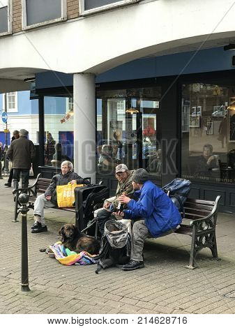 Carmarthen, Carmarthen-shire. United Kingdom. 17th November 2017. Two homeless men sitting on a bench in the town drinking a bottle of alcohol with a pet dog and belongings in a rucksack and case.