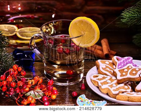 Christmas gluhwein glass mug and Christmas multicolored cookies on form stars on plate with fir branches. Glogg mug decoration lemon slice on wooden table. Treats and candels.