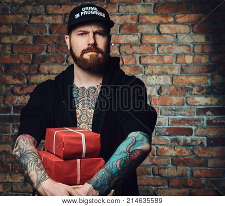 The positive Redbeard male holds Christmas gifts over the wall of a brick.