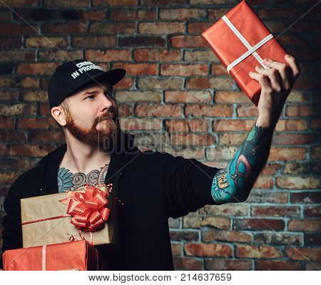 The positive Redbeard male holds Christmas gifts over the wall of a brick.