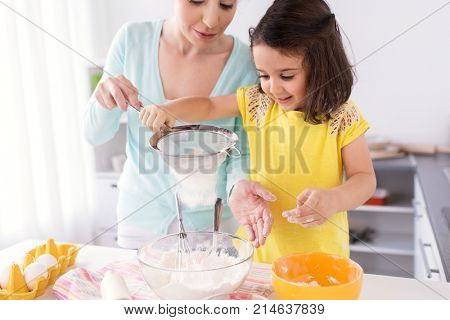 family, cooking, baking and people concept - happy mother and little daughter with sieve sifting flour and making dough at home kitchen