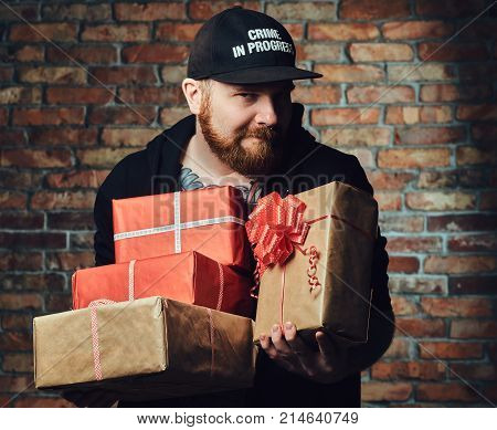 The positive Redbeard male holds Christmas gifts over the wall of a brick.