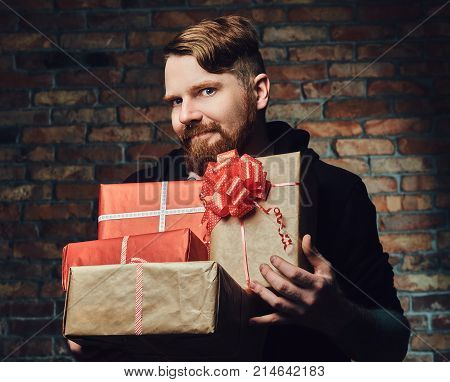 The positive Redbeard male holds Christmas gifts over the wall of a brick.