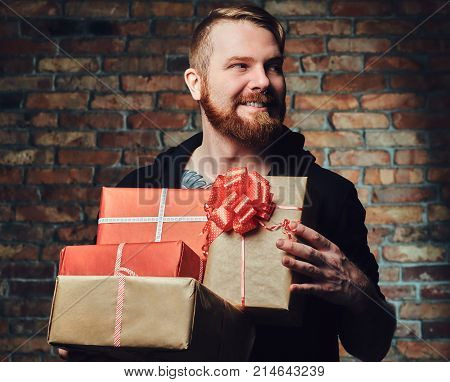 The positive Redbeard male holds Christmas gifts over the wall of a brick.