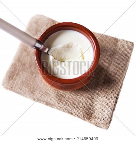 Sour cream or Cottage cheese curd in clay pot isolated on a white background. Traditional Cuajada yogurt cream with a spoon