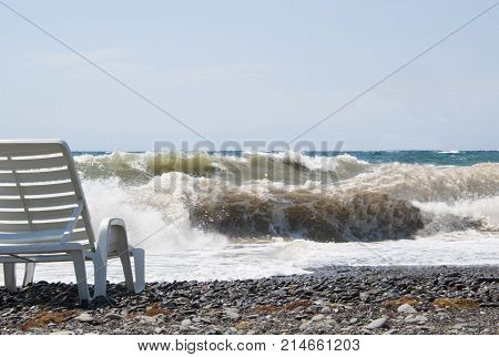 Chaise longue standing on the beach by the sea on a summer day. Big waves of the stormy sea. Sunny weather