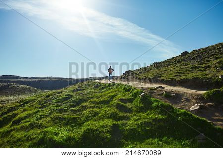 back view of woman traveler with small orange backpack on a walk in the Valley of the river of Hveragerdi Iceland. Hiking Tour of Reykjadalur Hot Springs